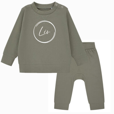 Kahki chillpakje, bestaande uit een top met ronde hals en drukknoopjes en broek met elastiek onderaan de broekspijpen en een elastische tailleband. De top is voorzien van naam en cirkel.